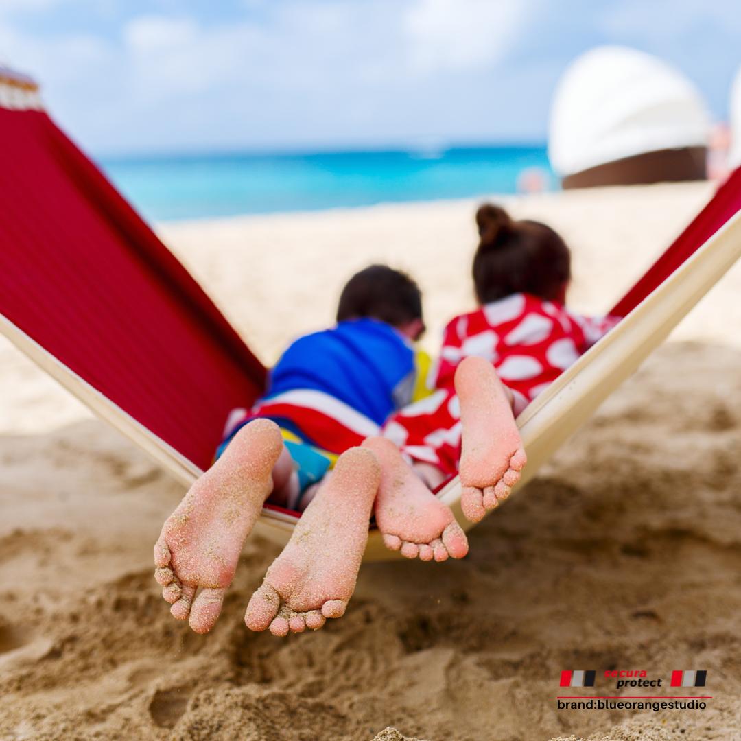 Zwei Kinder liegen auf einer Hängematte am Strand und zeigen die sandigen Füße